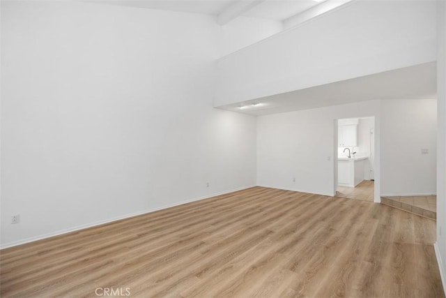 unfurnished room featuring beamed ceiling, a sink, baseboards, and light wood-type flooring
