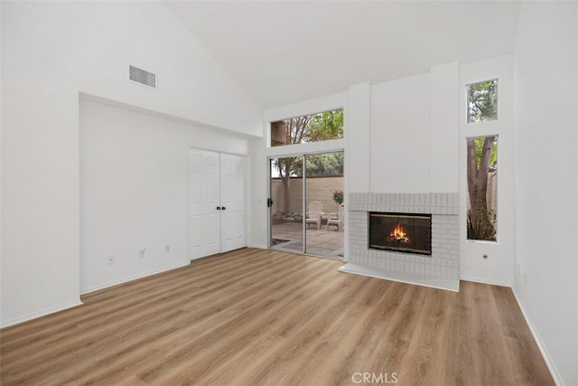 unfurnished living room featuring visible vents, light wood-style flooring, a fireplace, and high vaulted ceiling