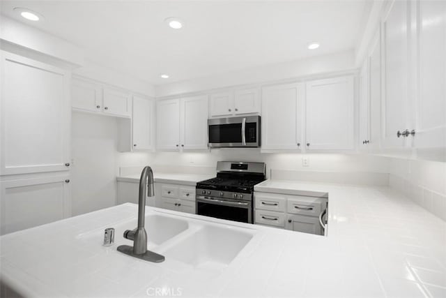 kitchen featuring white cabinets, tile counters, appliances with stainless steel finishes, and a sink