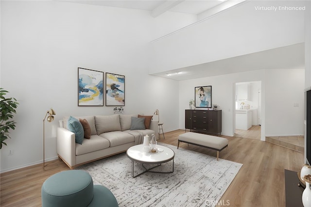 living room featuring vaulted ceiling with beams, baseboards, and light wood-style flooring