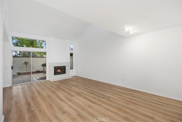 unfurnished living room with a brick fireplace, vaulted ceiling, and light wood-style flooring