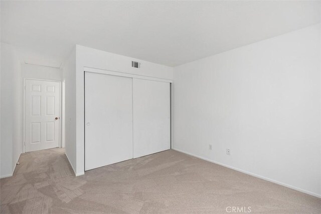 unfurnished bedroom featuring light colored carpet, visible vents, and a closet