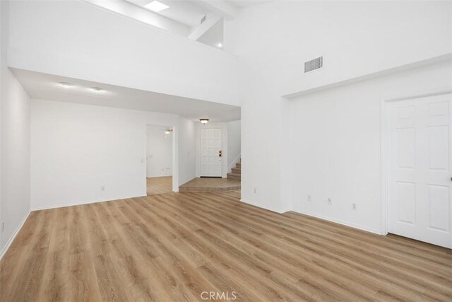 unfurnished living room with visible vents, beam ceiling, stairway, high vaulted ceiling, and light wood-style flooring