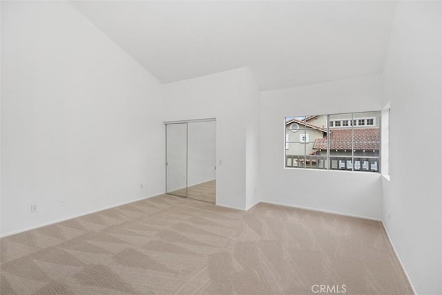 carpeted empty room featuring baseboards and high vaulted ceiling