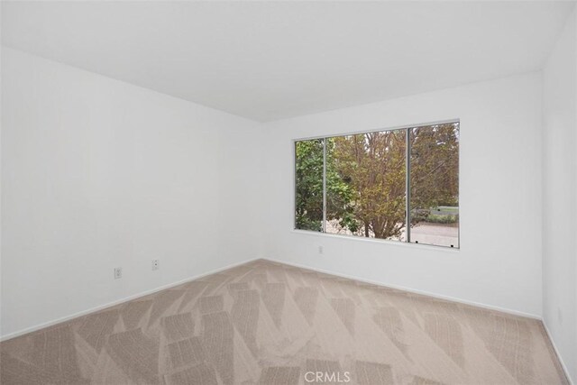 spare room with baseboards and light colored carpet