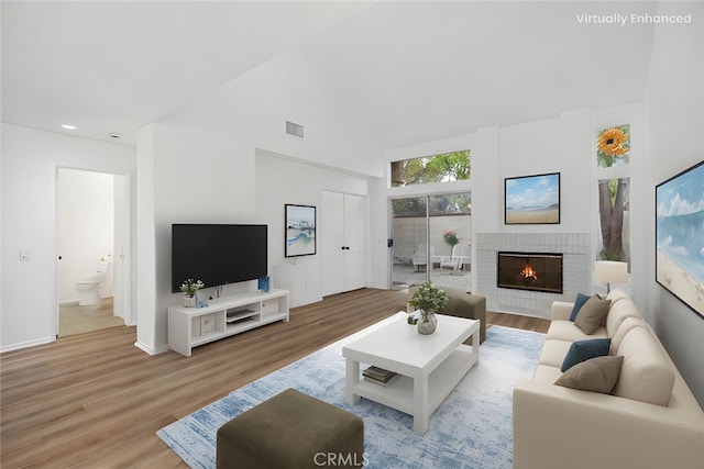 living room with a high ceiling, light wood finished floors, a fireplace, recessed lighting, and visible vents