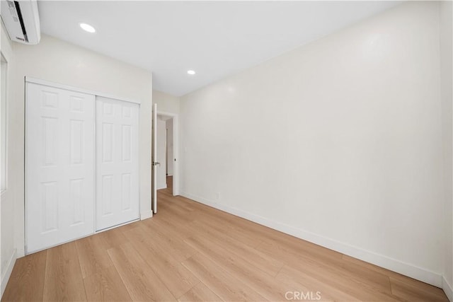 unfurnished bedroom featuring light wood-style floors, a wall mounted AC, baseboards, and a closet