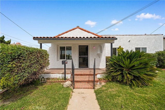 view of front of property featuring stucco siding, a tiled roof, and a front lawn