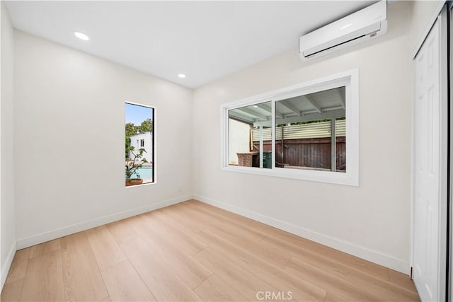 unfurnished room with a wall mounted air conditioner, recessed lighting, light wood-type flooring, and baseboards
