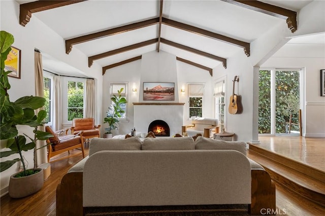 living room featuring a warm lit fireplace, vaulted ceiling with beams, and wood finished floors