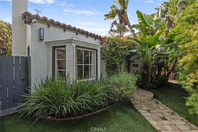 view of side of property with fence, stucco siding, and a tiled roof