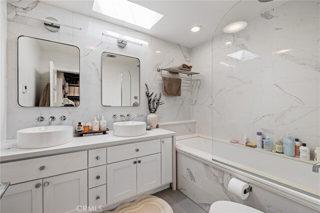 bathroom featuring double vanity, a sink, a skylight, and a combined bath / shower with marble appearance