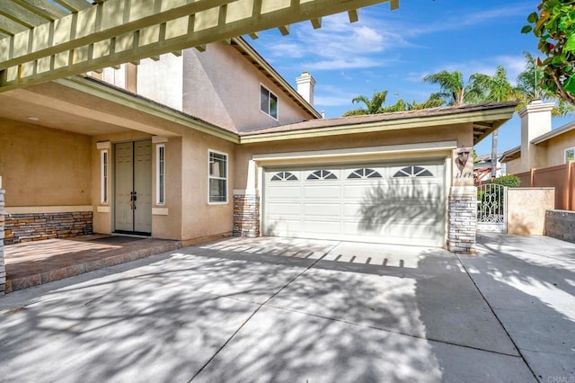 exterior space with stone siding, fence, an attached garage, concrete driveway, and stucco siding