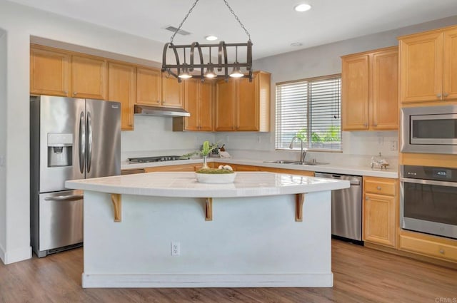 kitchen with a kitchen island, appliances with stainless steel finishes, under cabinet range hood, tile countertops, and a sink