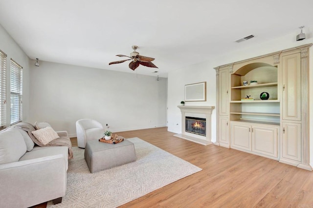 living area featuring visible vents, light wood-style flooring, a glass covered fireplace, and a ceiling fan