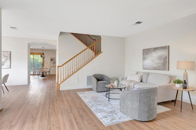 living room with arched walkways, stairs, visible vents, and light wood-style floors