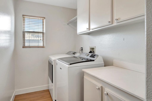 laundry area with light wood-style floors, cabinet space, baseboards, and washer and dryer