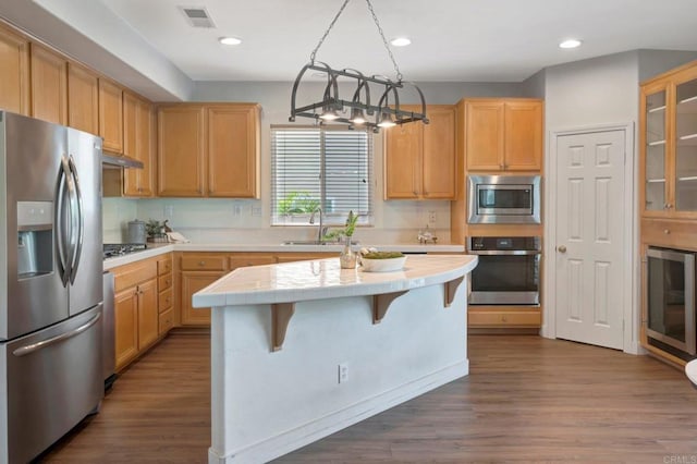 kitchen with stainless steel appliances, a center island, a sink, beverage cooler, and visible vents