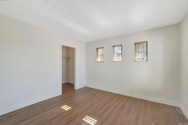unfurnished bedroom with baseboards, a spacious closet, wood finished floors, and a closet