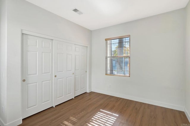 unfurnished bedroom with baseboards, visible vents, a closet, and wood finished floors