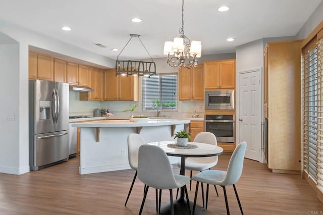 kitchen with light countertops, under cabinet range hood, a kitchen island, a notable chandelier, and appliances with stainless steel finishes