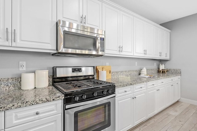 kitchen featuring light wood-style flooring, white cabinetry, baseboards, light stone countertops, and appliances with stainless steel finishes