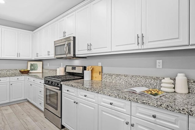 kitchen featuring white cabinetry, light stone counters, stainless steel appliances, and light wood-style flooring