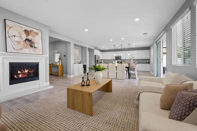 living area featuring light wood-style floors, a glass covered fireplace, and recessed lighting