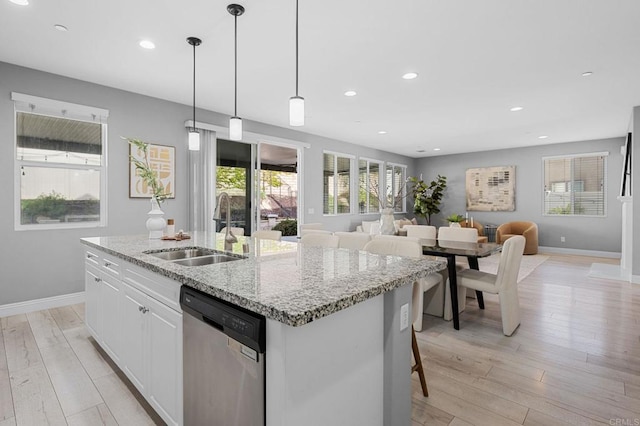 kitchen with a sink, light wood-type flooring, a kitchen island with sink, dishwasher, and baseboards