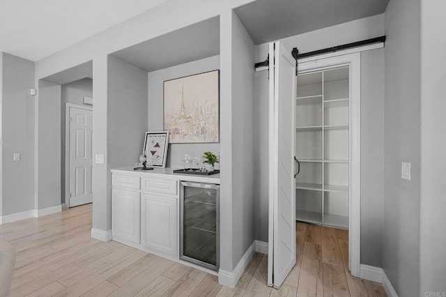 bar with a dry bar, baseboards, light wood-type flooring, and beverage cooler