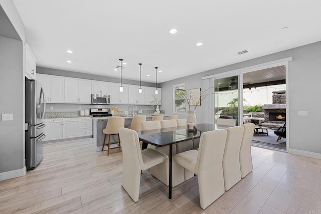 dining area featuring light wood-style floors, a stone fireplace, visible vents, and recessed lighting
