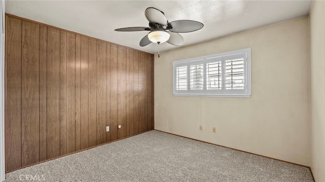 carpeted empty room with wooden walls, baseboards, and ceiling fan
