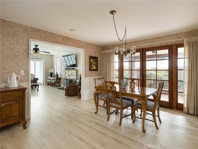 dining room featuring wallpapered walls, a wainscoted wall, ornamental molding, and light wood-style flooring