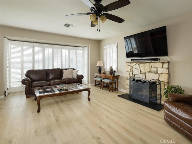 living room featuring a fireplace, wood finished floors, baseboards, visible vents, and ceiling fan
