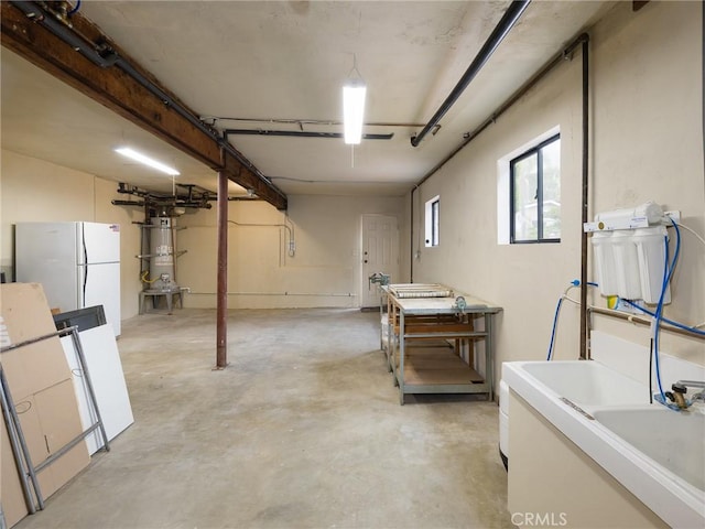 basement with strapped water heater, a garage, and freestanding refrigerator