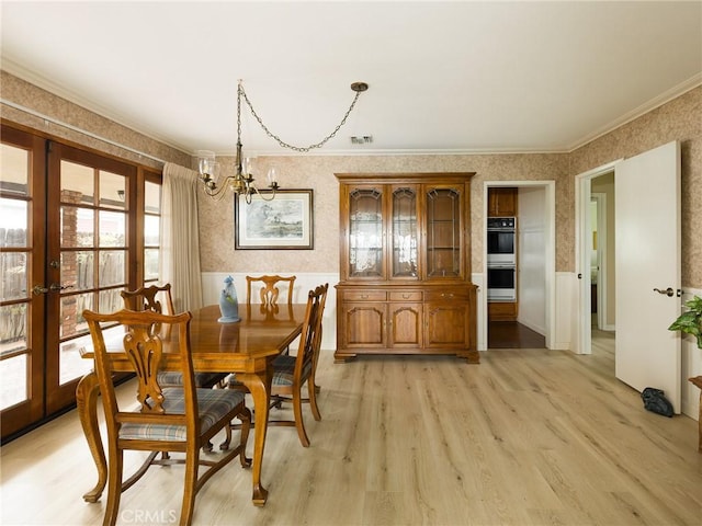 dining space with a chandelier, crown molding, wallpapered walls, light wood-style floors, and french doors