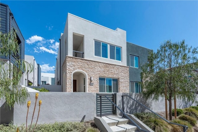 contemporary home with stucco siding, stone siding, and a fenced front yard
