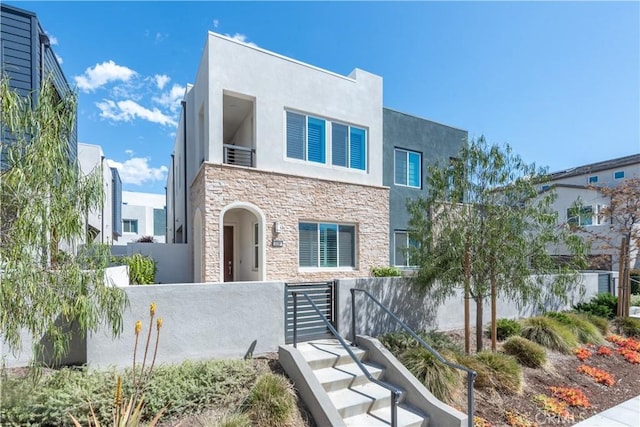 contemporary house with a fenced front yard, stucco siding, and stone siding