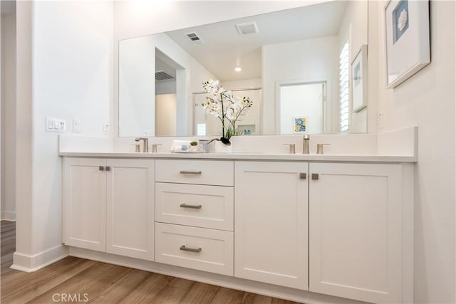 bathroom featuring visible vents, baseboards, double vanity, and wood finished floors
