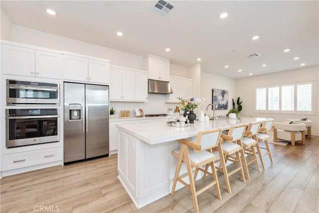 kitchen featuring visible vents, under cabinet range hood, light wood-style floors, and stainless steel appliances