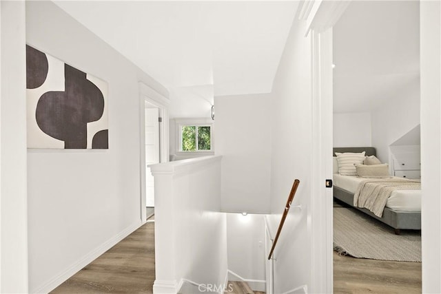 hall with wood finished floors, baseboards, and an upstairs landing