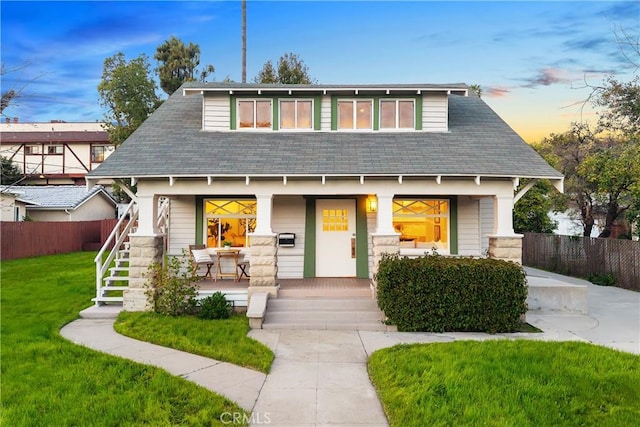 bungalow featuring a lawn, stairs, covered porch, and fence