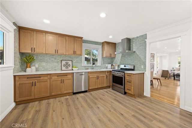 kitchen with stainless steel appliances, wall chimney range hood, a sink, light wood-type flooring, and tasteful backsplash