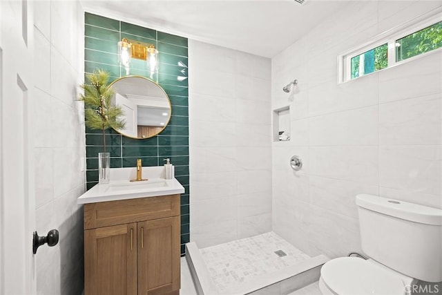full bath featuring a tile shower, tile walls, toilet, and vanity