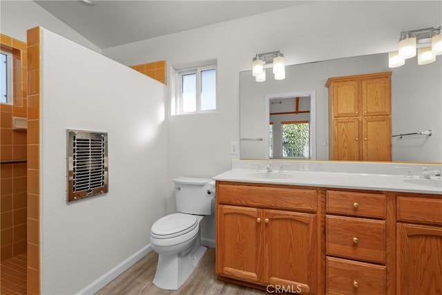 bathroom with toilet, a sink, tiled shower, double vanity, and wood finished floors