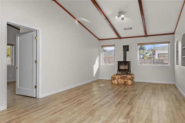 unfurnished living room with lofted ceiling with beams, light wood-type flooring, visible vents, baseboards, and a wood stove