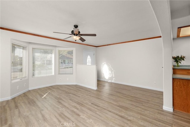 empty room featuring a ceiling fan, baseboards, crown molding, and light wood-type flooring