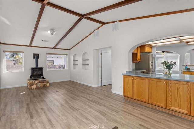 unfurnished living room featuring lofted ceiling with beams, a wood stove, light wood finished floors, arched walkways, and baseboards