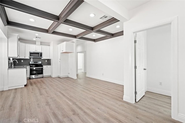 kitchen with beam ceiling, a sink, appliances with stainless steel finishes, light wood-type flooring, and visible vents