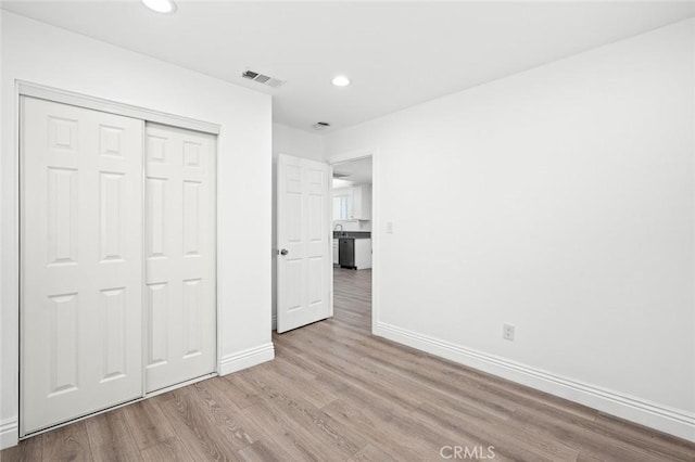 unfurnished bedroom with a closet, wood finished floors, baseboards, visible vents, and recessed lighting
